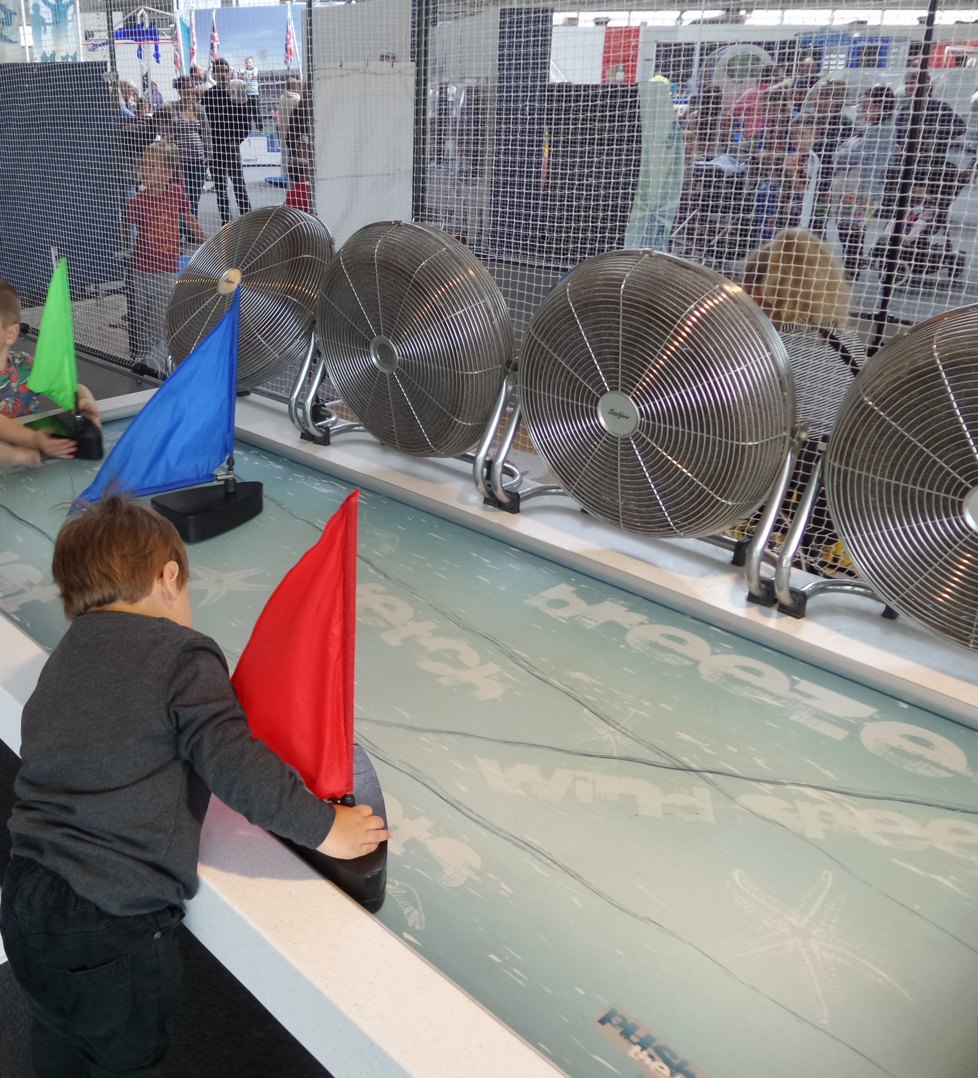 fans blowing sail boat models on water