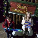 kids holding their gifts from Santa next to the Santa's Grotto sign