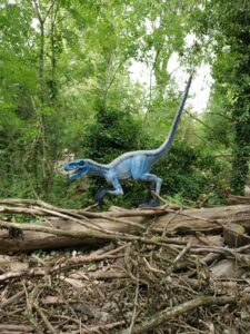 Blue dinosaur stood on logs in woods