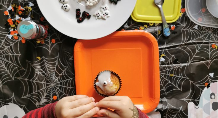 Looking down at table with child's hands decorating cupcake