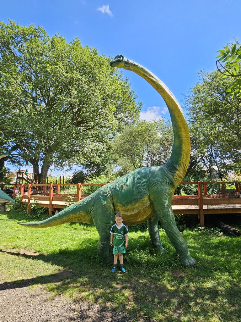 Child stood in front of large dinosaur model outdoors