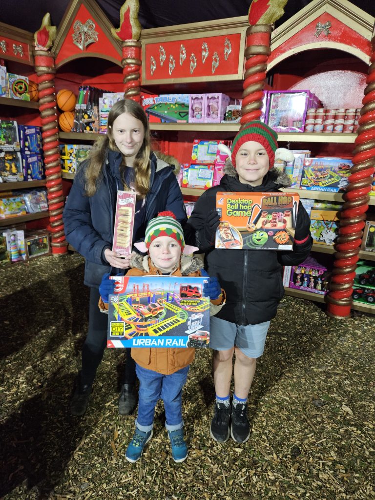 3 children stood holding toys in Santa's toy shop