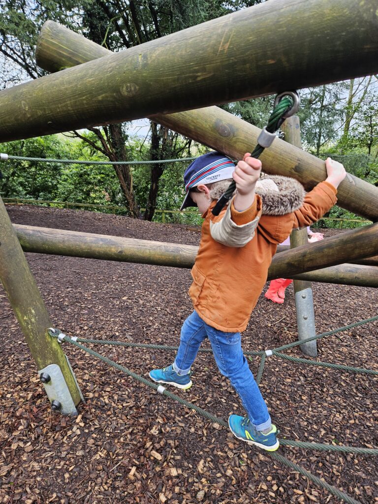 Young child balancing along rope on playframe