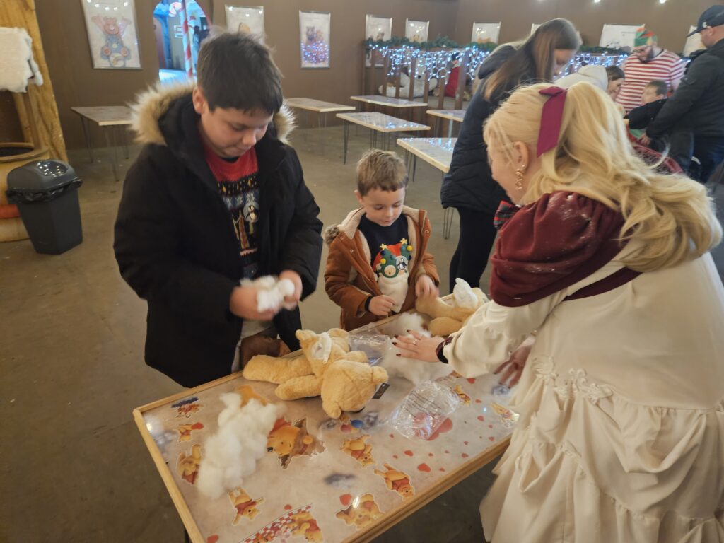Elf helping two children stuff fluff in their teddy bears