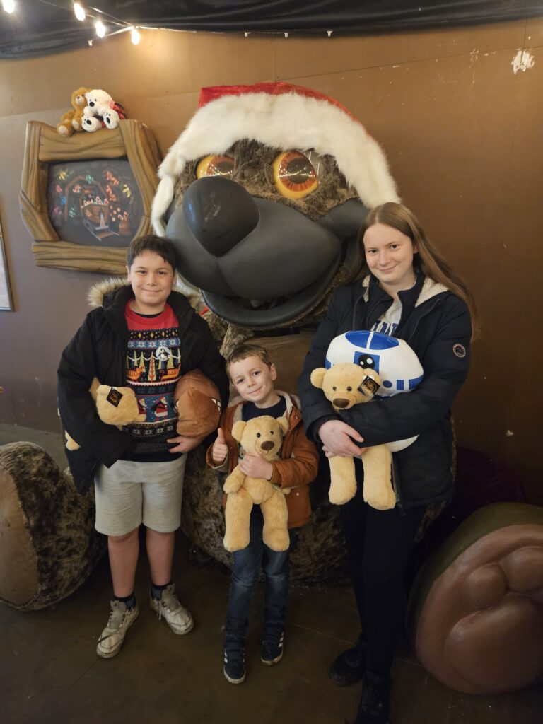 3 children holding teddy bears stood in front of giant teddy bear